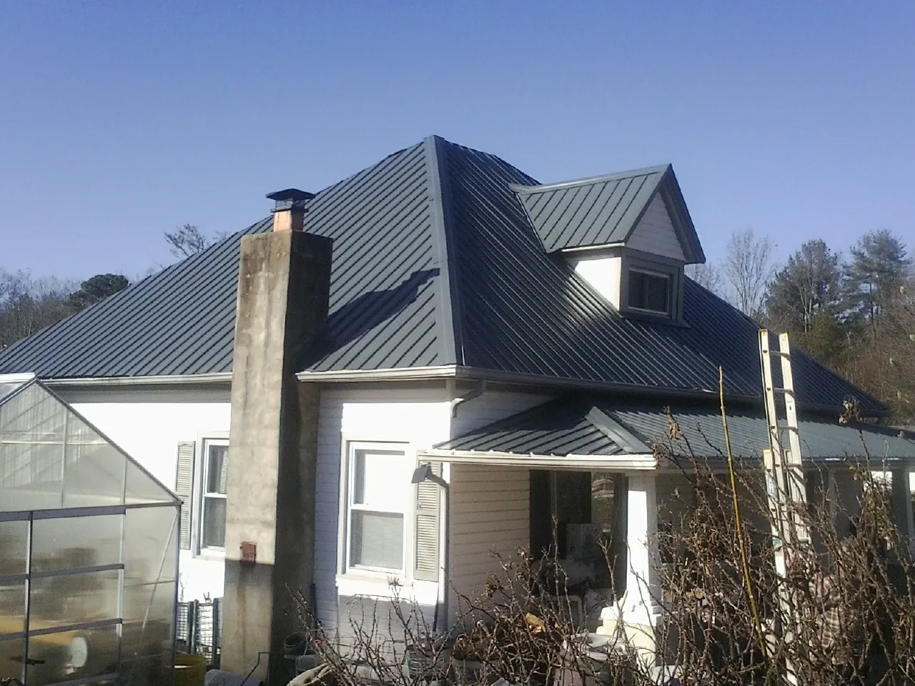 Dark blue standing seam metal roof on a white farmhouse with dormer — Slate & Tile Roof Repair by Roofing Brothers in Centerview