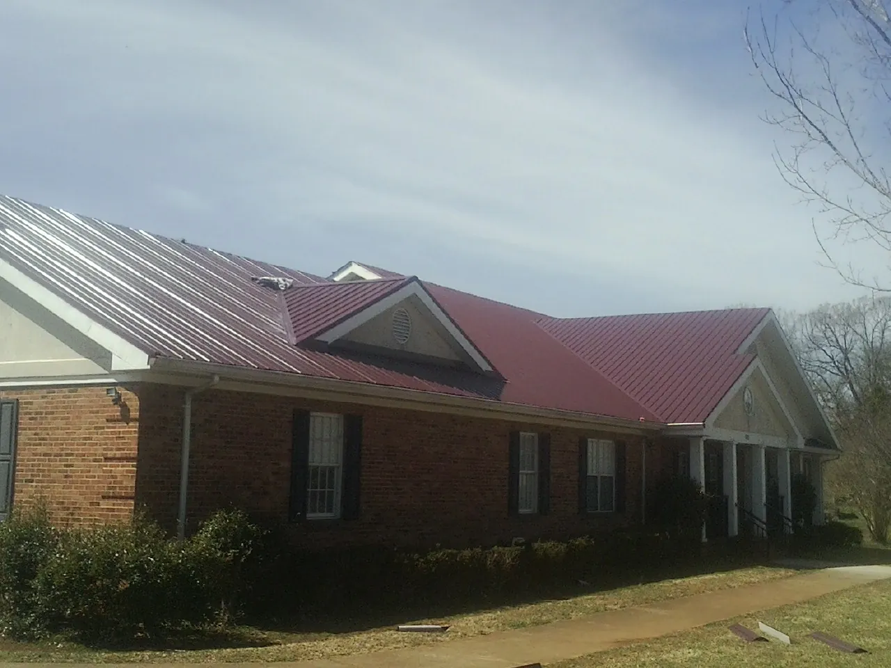 Red metal roof with gabled entries on a long brick building, from a Hail Damage Roof Repair job in Centerview