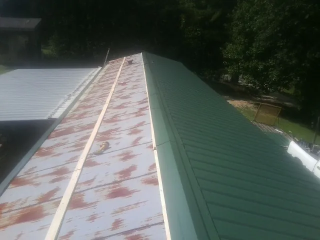 Old rusted panels beside newly installed green metal roofing — Wind Damage Roof Repair by Roofing Brothers in Centerview