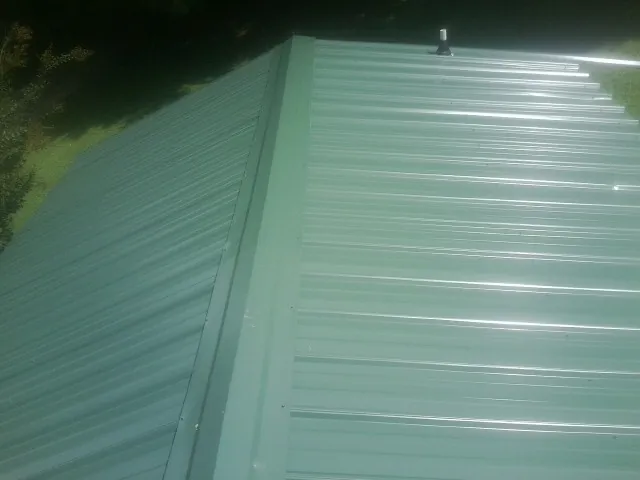 New green metal panels meeting at the ridge of a roof — Flat Roof Repair work by our crew in Centerview