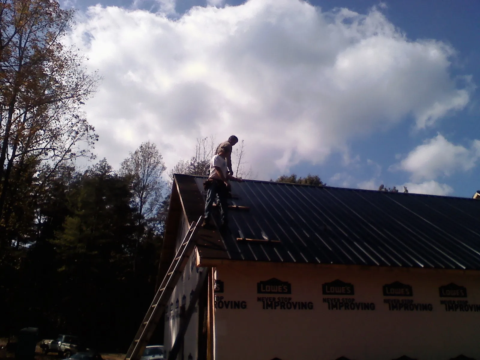 Roofer fastening dark metal panels high against a cloudy sky, from a Roof Inspection job in Centerview