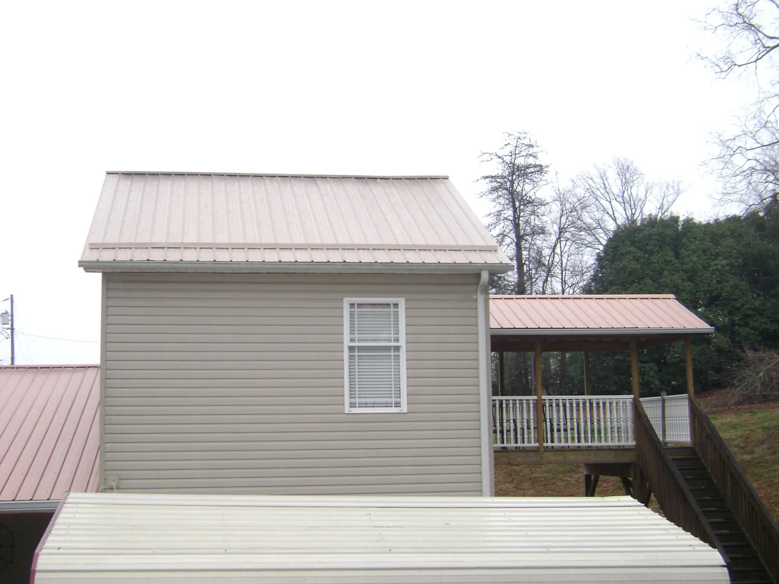 Tan metal roofs on a two story addition and attached porch, from a Roof Replacement job in Centerview